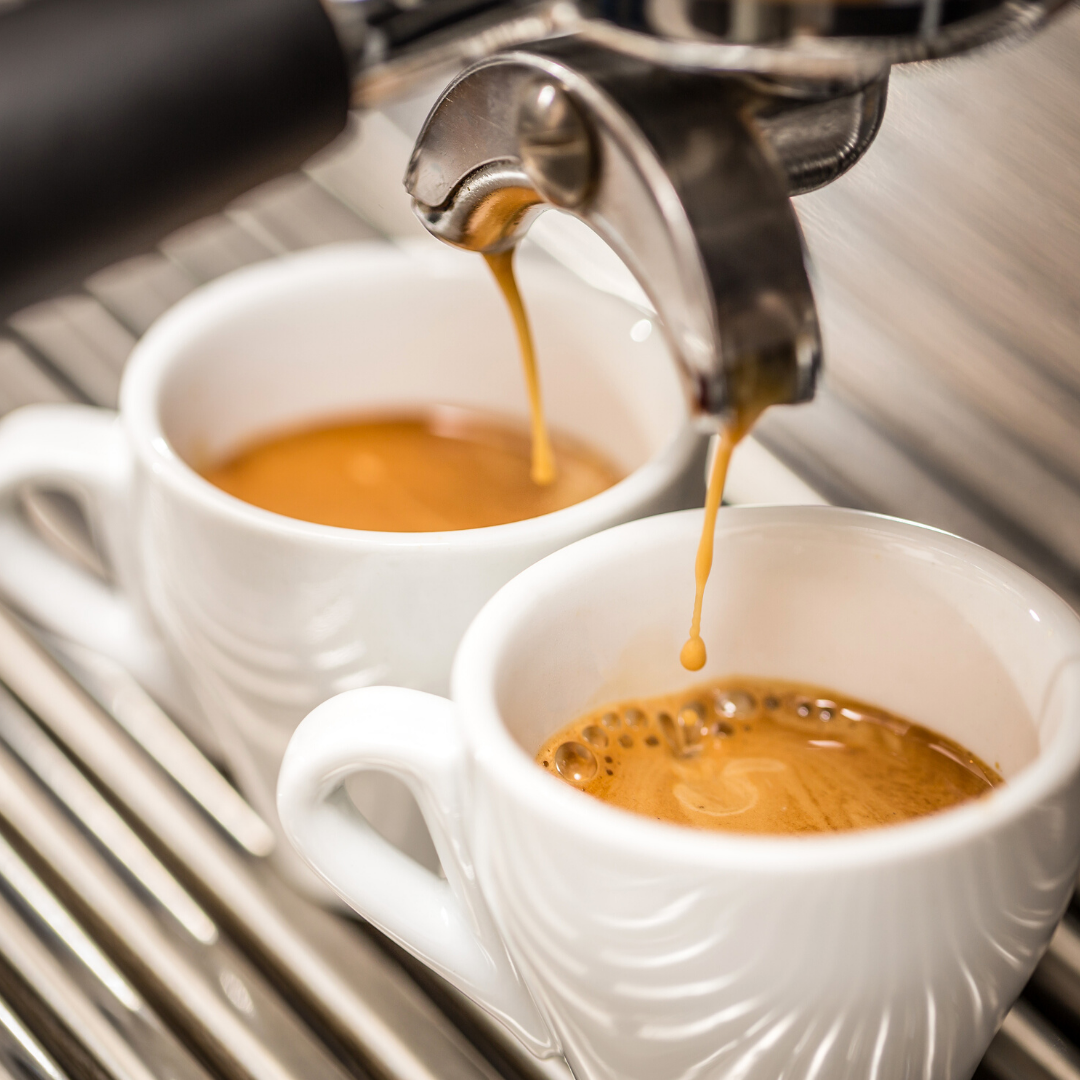 Espresso being poured into two white cups from a coffee machine.