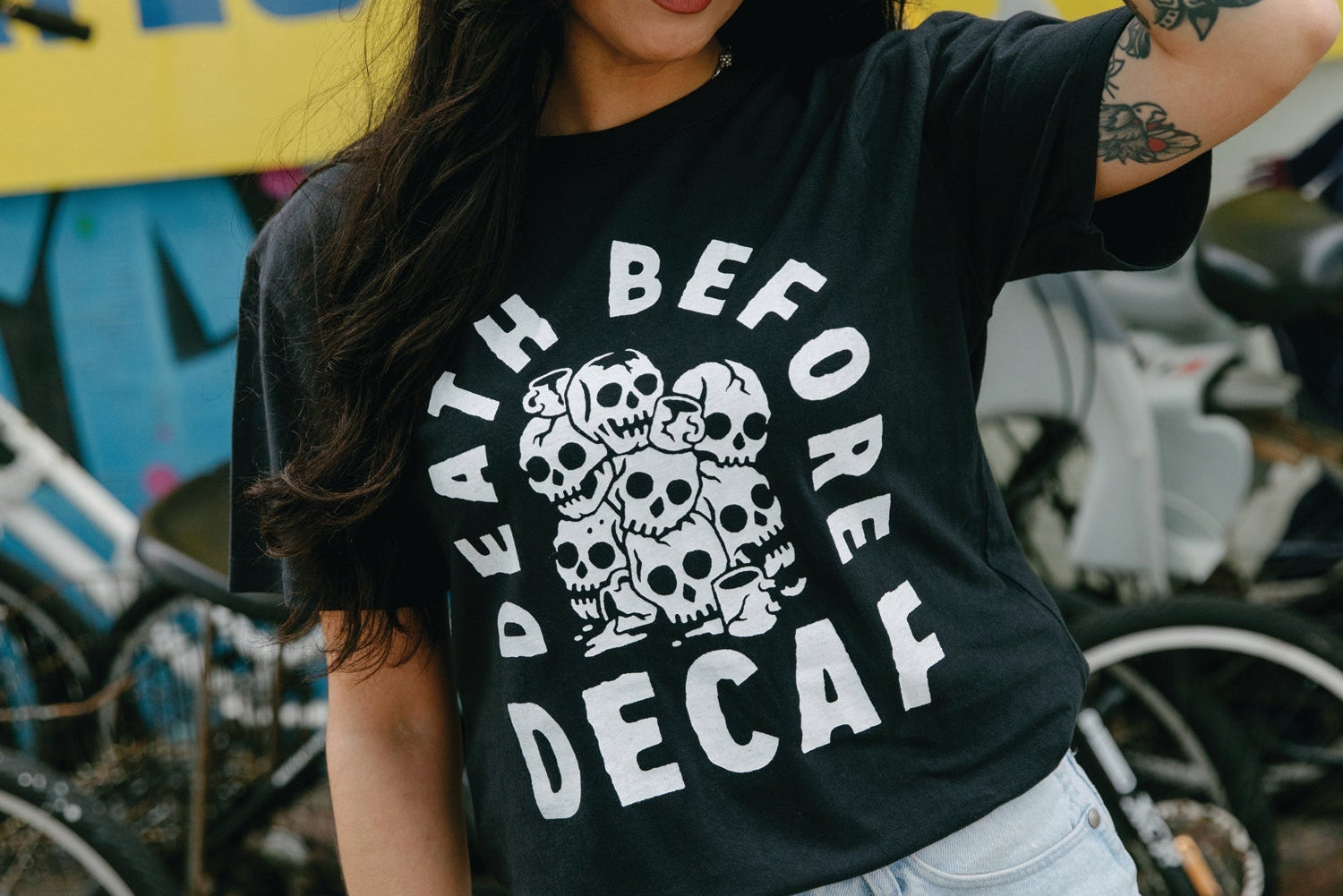Woman wearing a black t-shirt with 'Death Before Decaf' graphic in an urban setting.